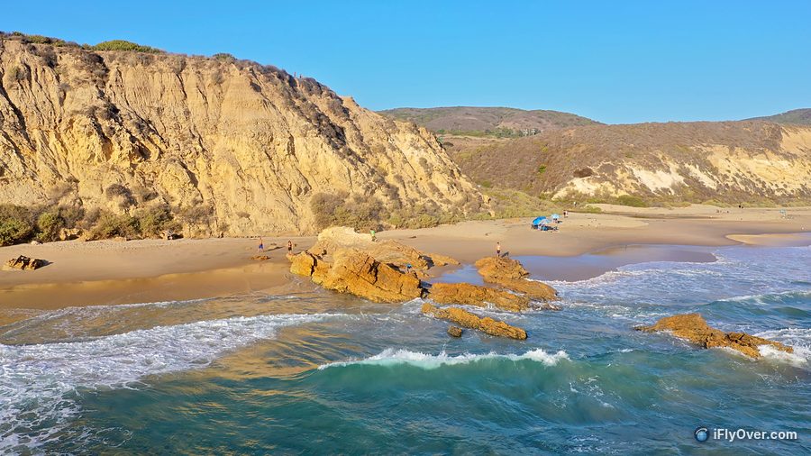 Low aerial photo of a beach cove with a sandstone bluff, rocks and waves