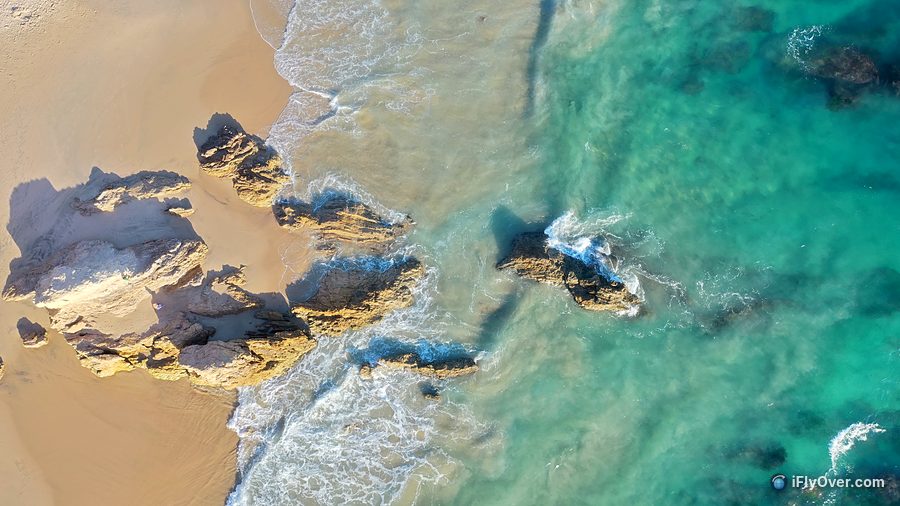 Top-down drone photo of sand, rocks and clear turquoise water